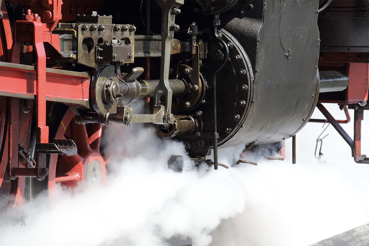 Close up of the cylinder of a steam locomotive surrounded by steam