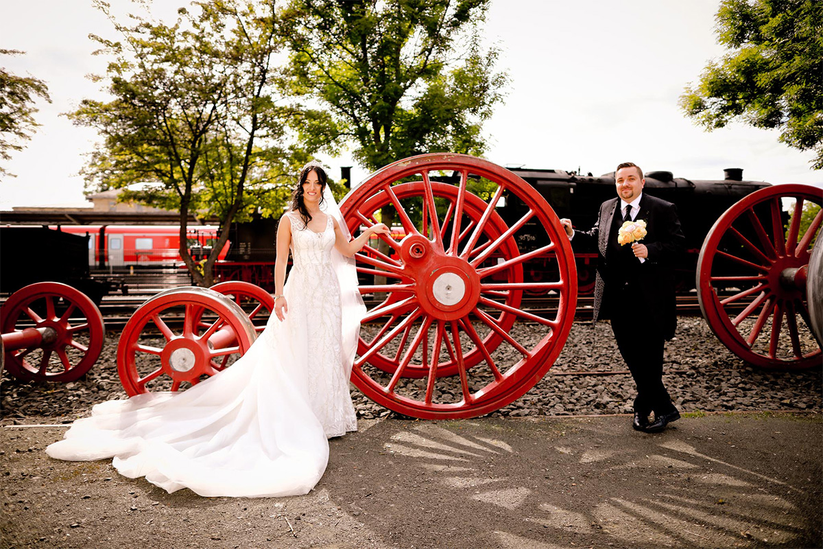 Ein Hochzeitspaar posiert für ein Shooting vor einem Satz ausgestellter Laufräder einer Dampflok