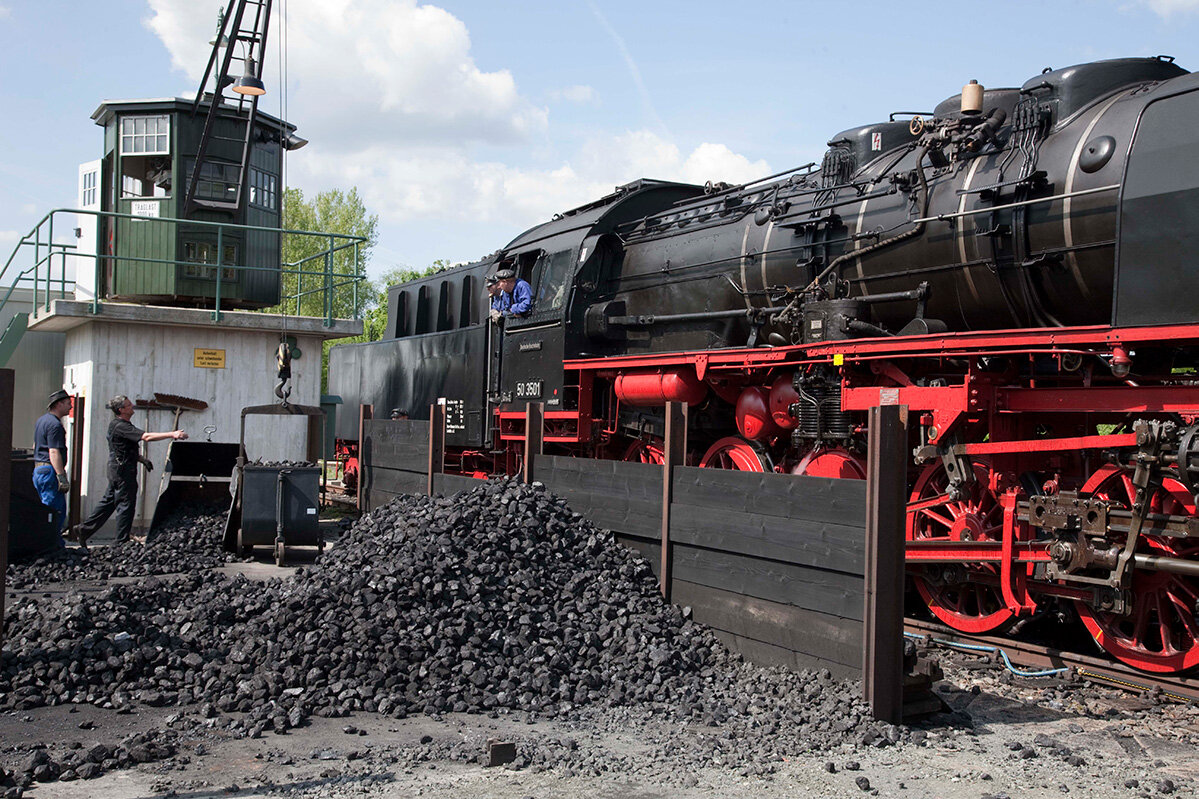 A crane is loaded with coal to supply it to the steam locomotive next to it