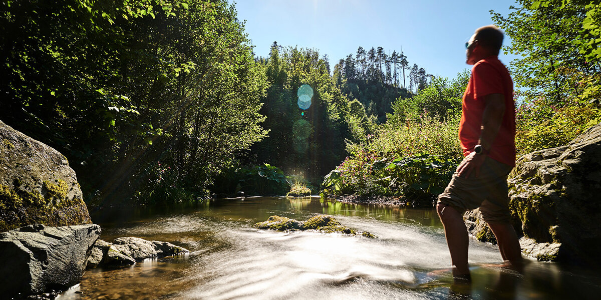 Ein Mann steht mit hochgekrempelten Hosen in einem Flußlauf in der Steinachklamm