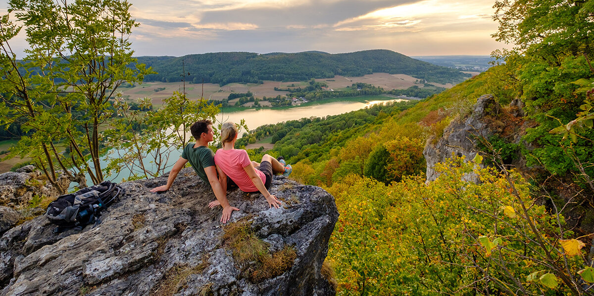 Ein Paar sitzt auf einem Felsvorsprung und genießt den weiten Ausblick ins Tal