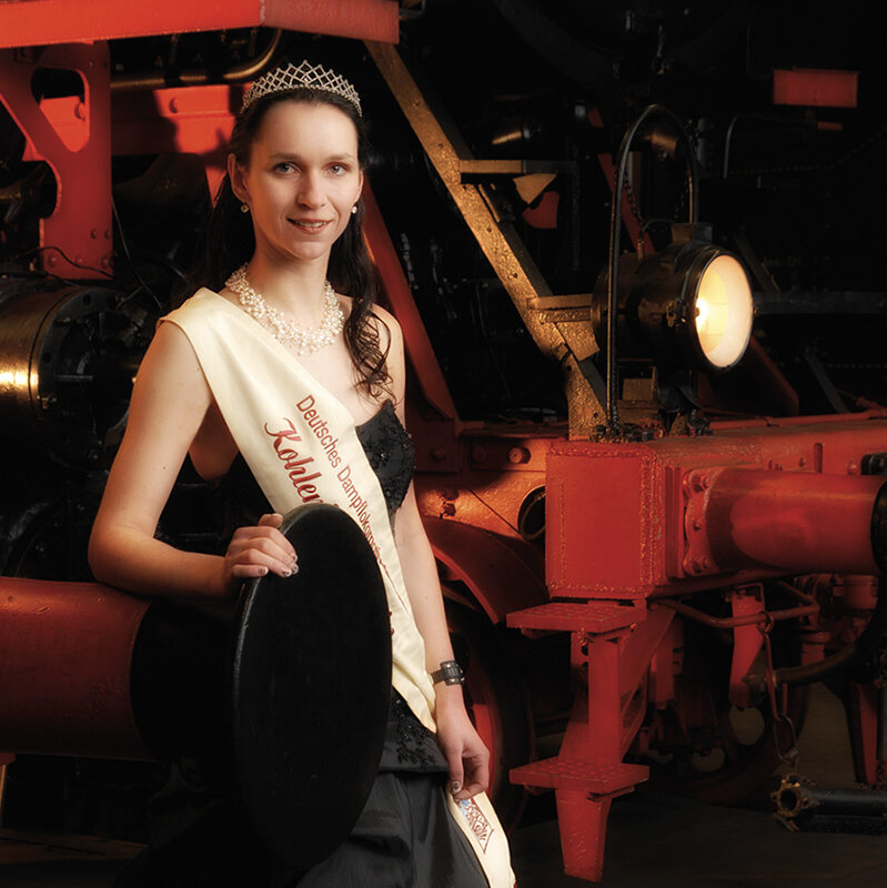 The princess of the coal yard Anja I. is wearing a sash and posing in front of a steam locomotive