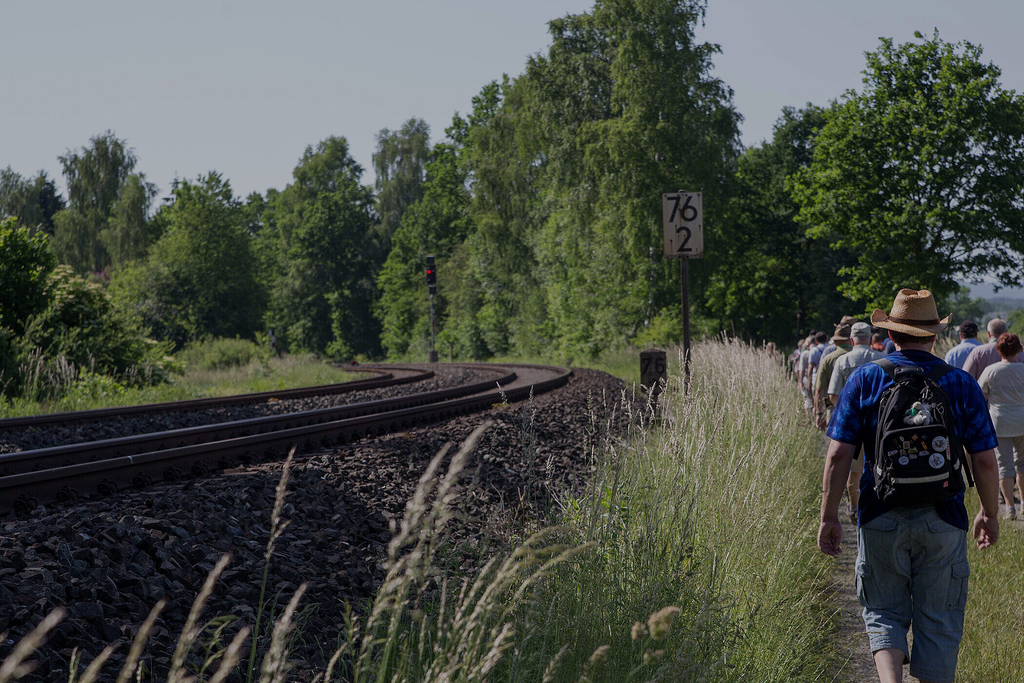 Eine Gruppe Eisenbahnbegeisterter wandert an einem sonnigen Tag entlanf der Schienen