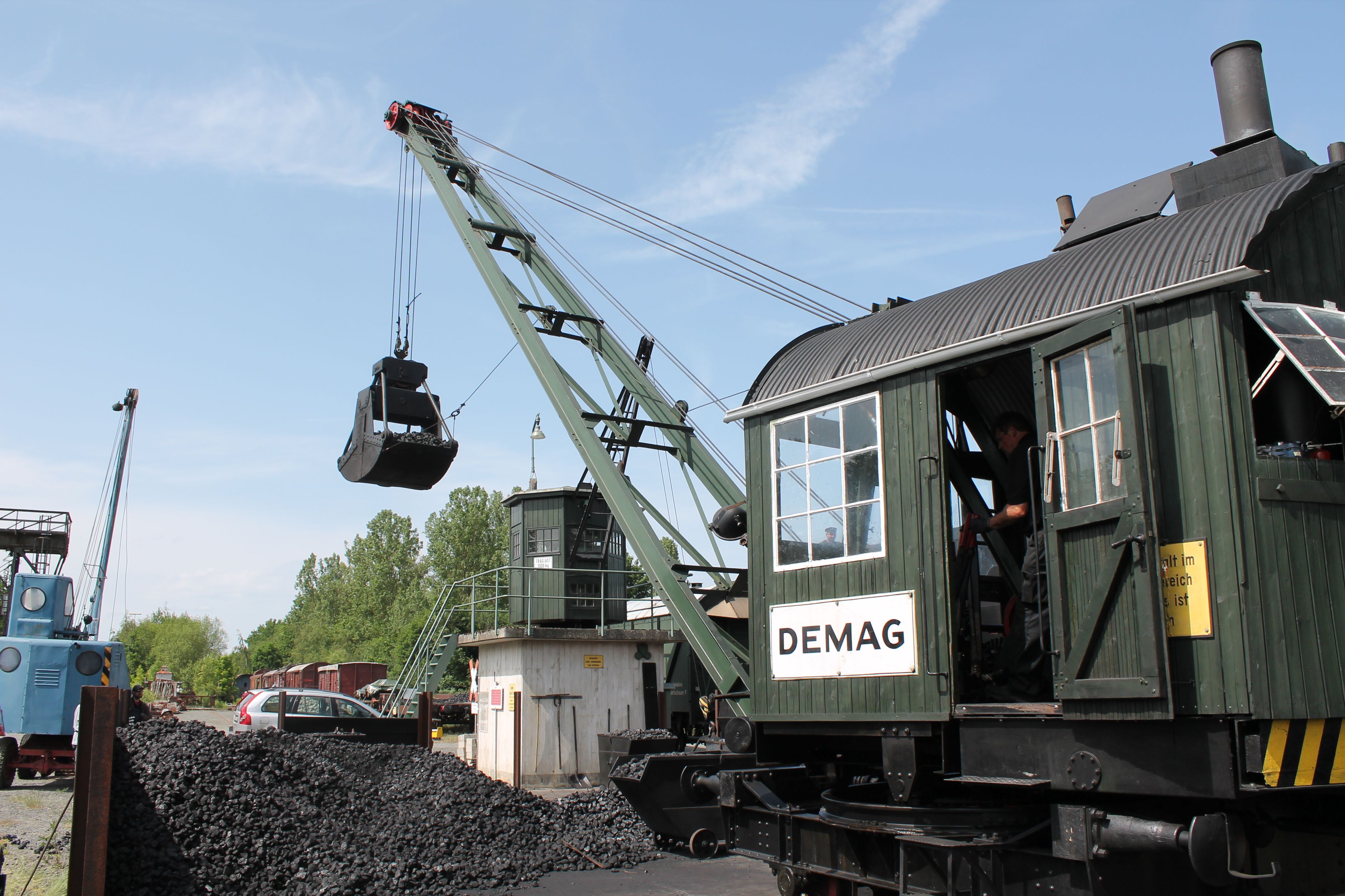 A green steam crane lifting lumps of coal from a pile with a shovel