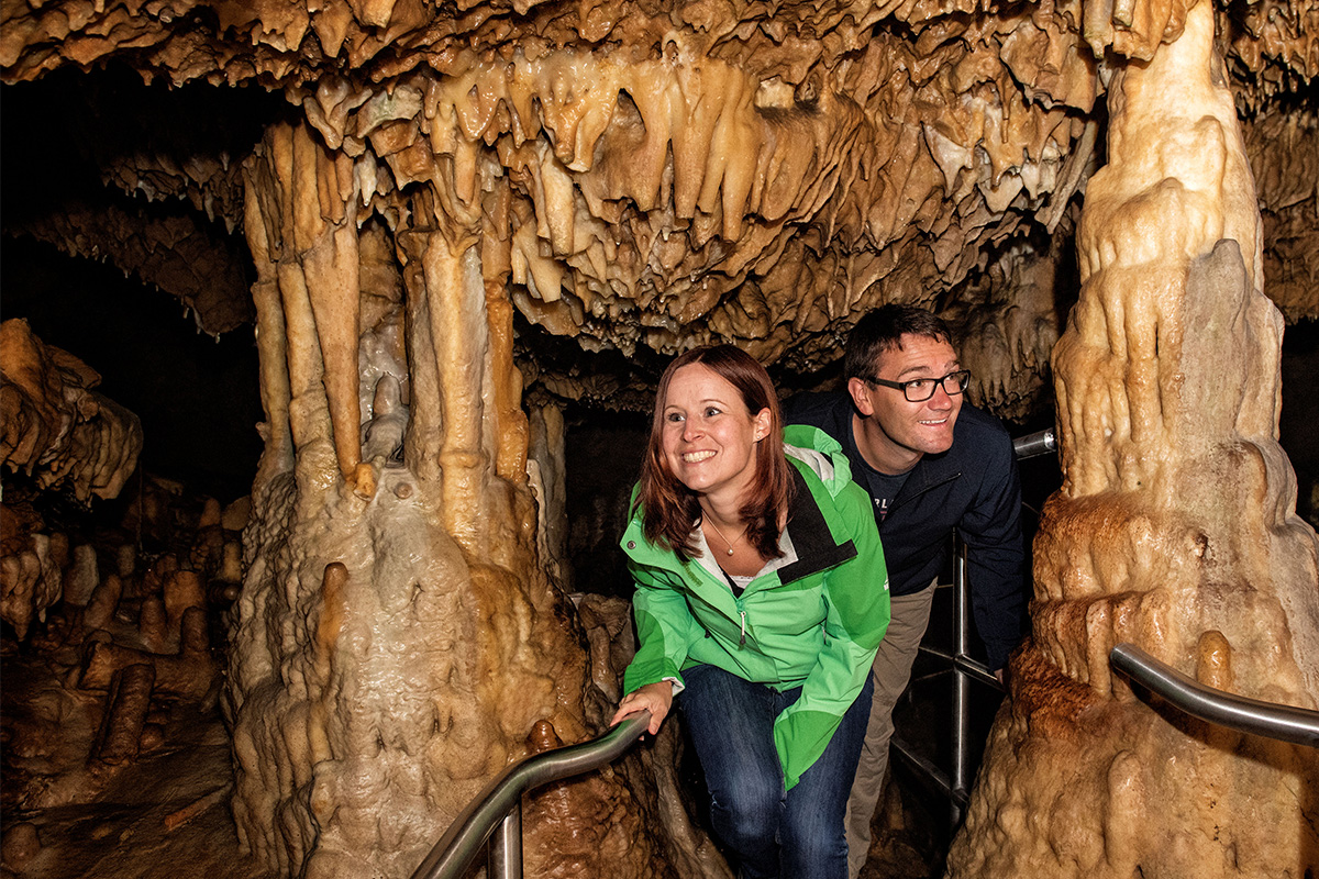 Ein Paar geht gebückt durch eine schmale Stelle in einer Tropfsteinhöhle