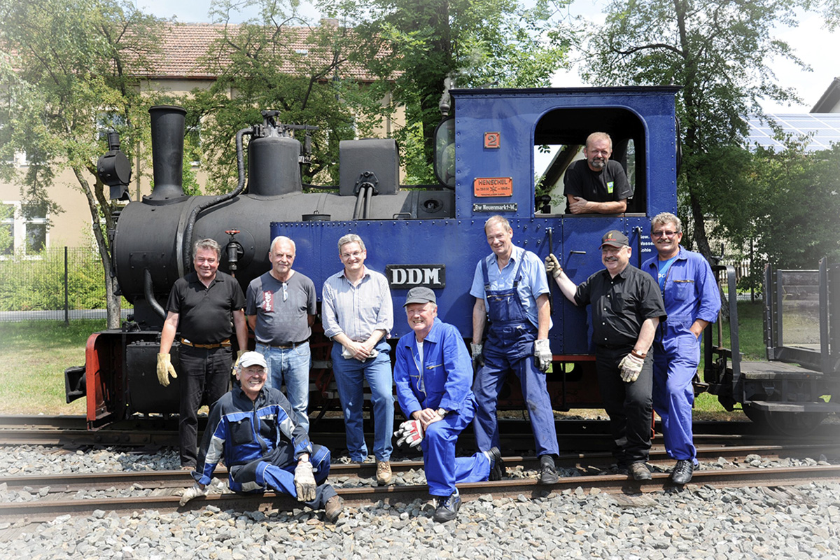 Gruppe von Männern vor einer blauen Lok mit DDM-Aufschrift