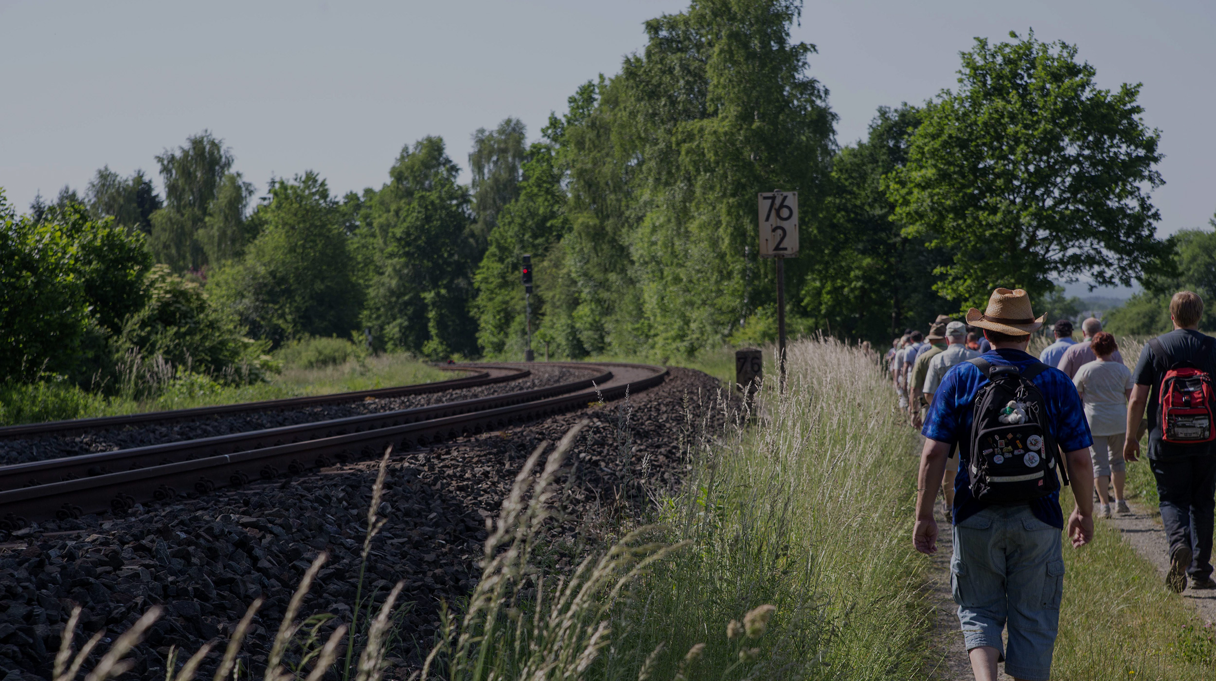Eine Gruppe Eisenbahnbegeisterter wandert an einem sonnigen Tag entlanf der Schienen