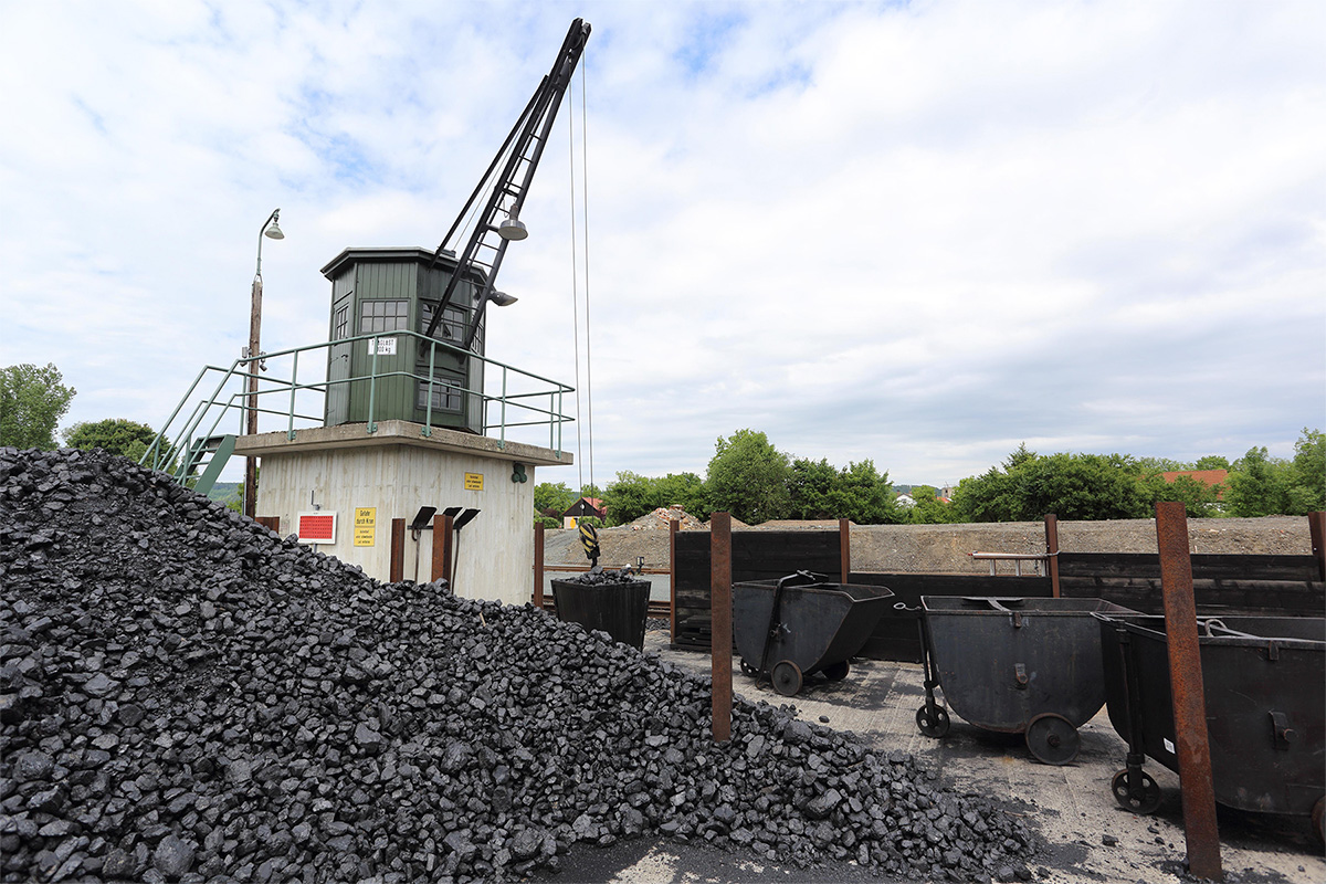 A small crane behind a large pile of coal in the foreground