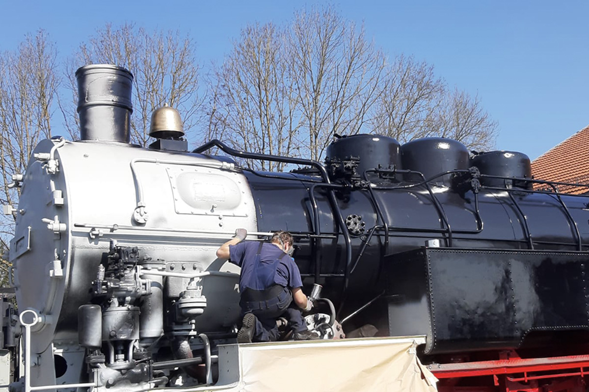 A person is painting a steam locomotive with black coating